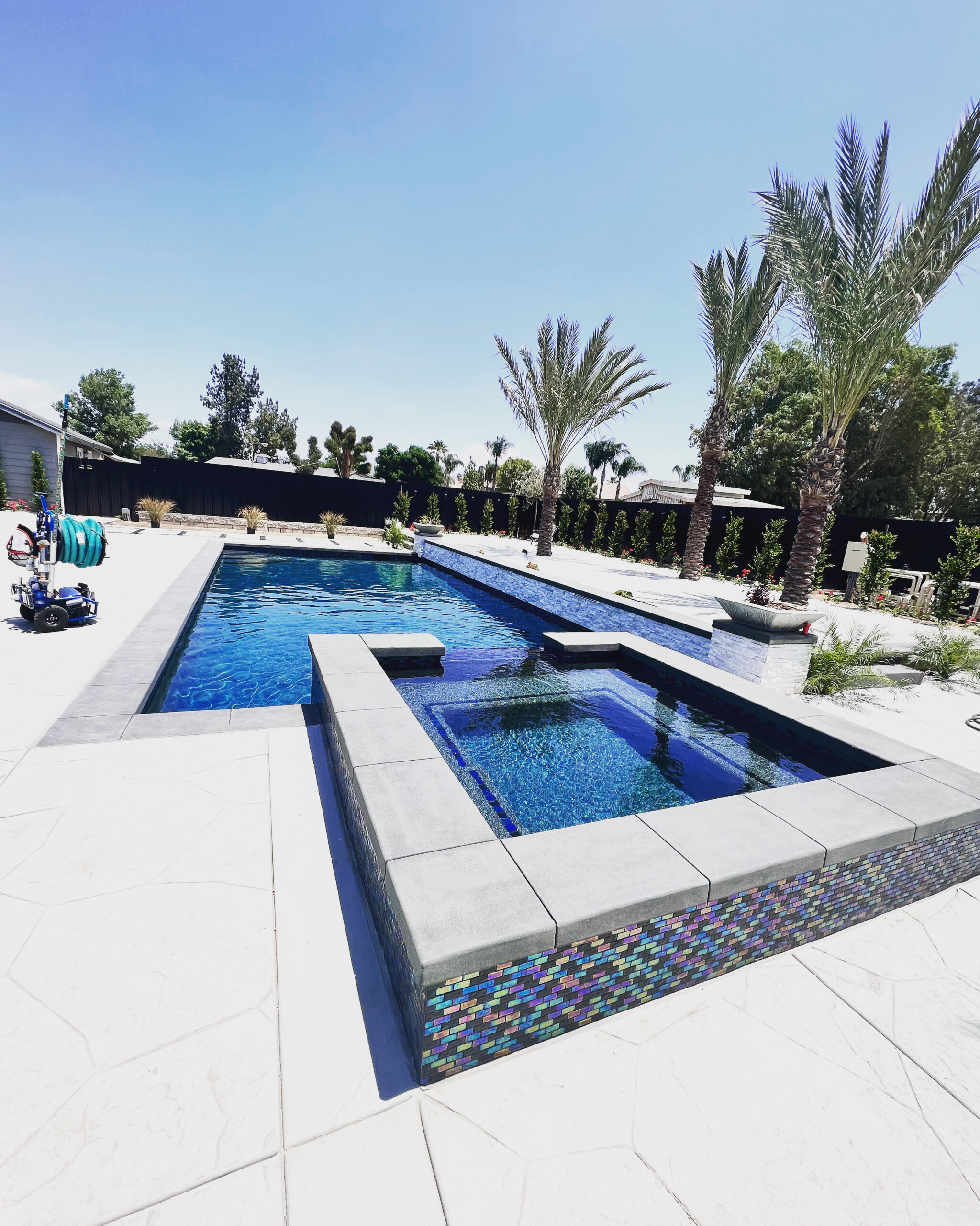 Luxury backyard pool with raised spa, modern tile detailing, expansive decking, and palm trees creating a resort-style outdoor space.