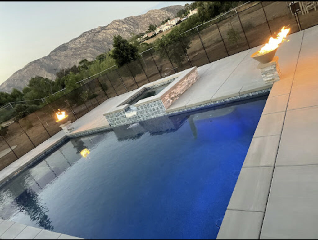 Luxury backyard pool with raised spa, cascading water feature, and decorative fire bowls set against scenic mountain views.