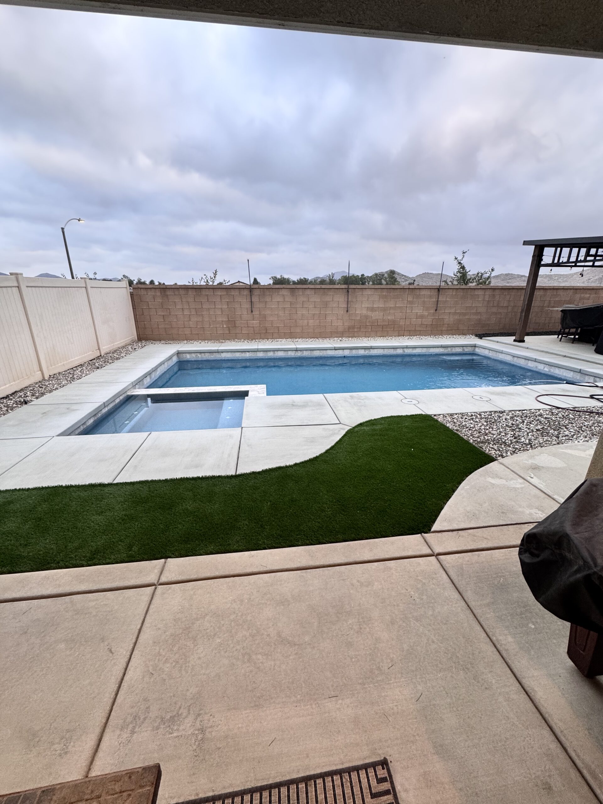 Modern backyard featuring a custom swimming pool with integrated spa, artificial turf accents, and clean concrete decking for a low-maintenance outdoor space. Pool Builder
