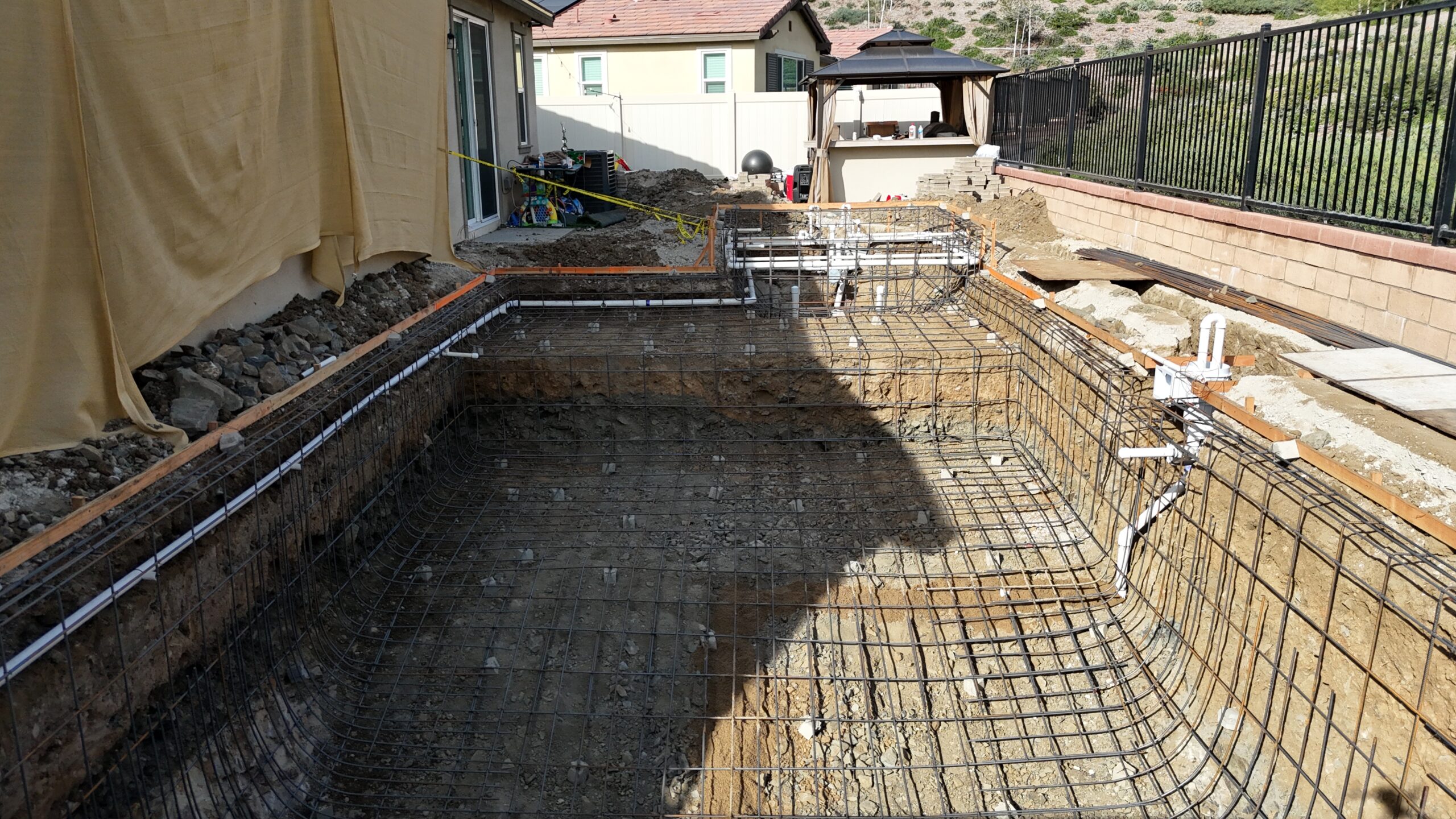 In-ground pool construction showing steel rebar framework and plumbing installation before gunite, preparing the structure for a durable custom swimming pool.